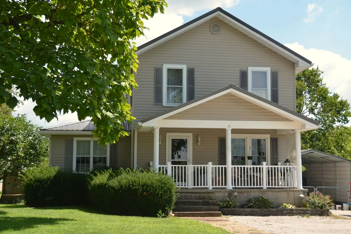 Two-story house with beige siding, gray shutters and a white gabled front porch with railings