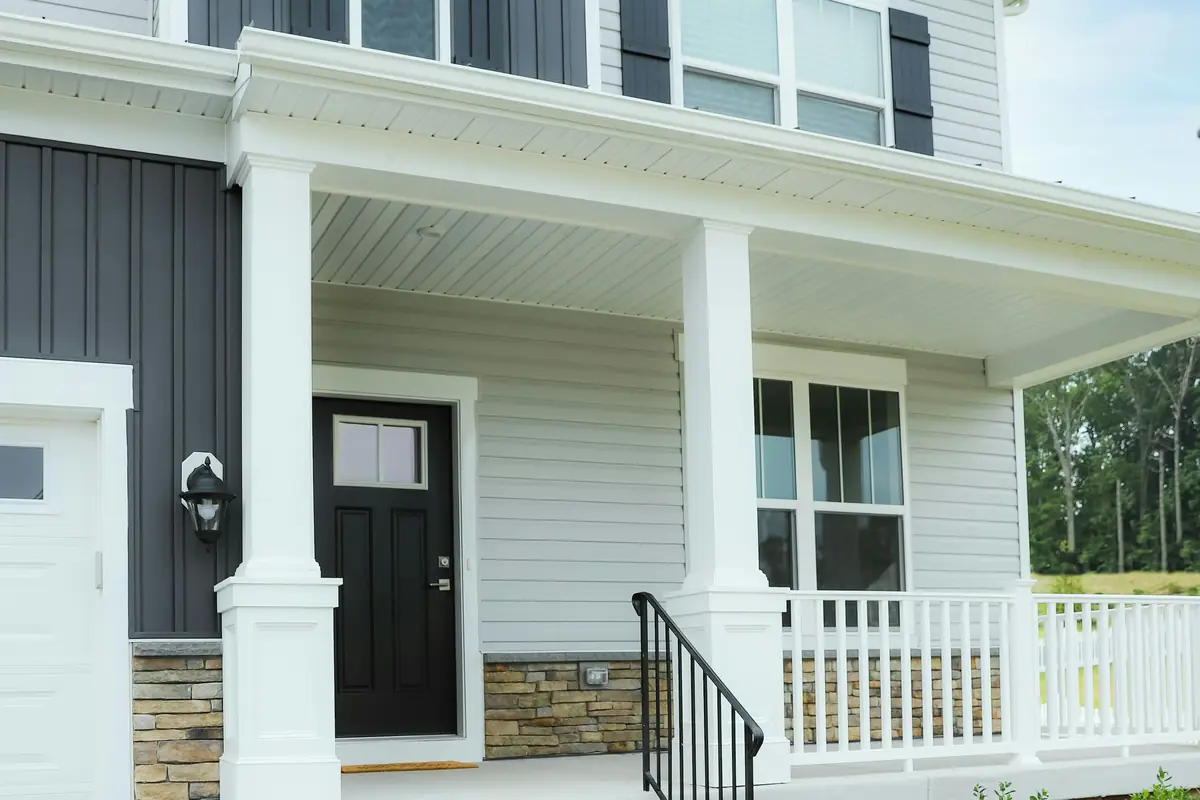 Two-story house with light gray lap siding, charcoal board-and-batten, black shutters and door, and a white-columned porch