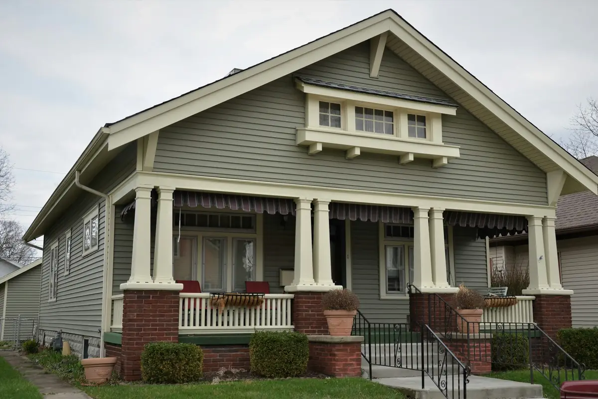 Craftsman bungalow with sage-green lap siding, cream trim and a front porch with tapered columns on brick piers