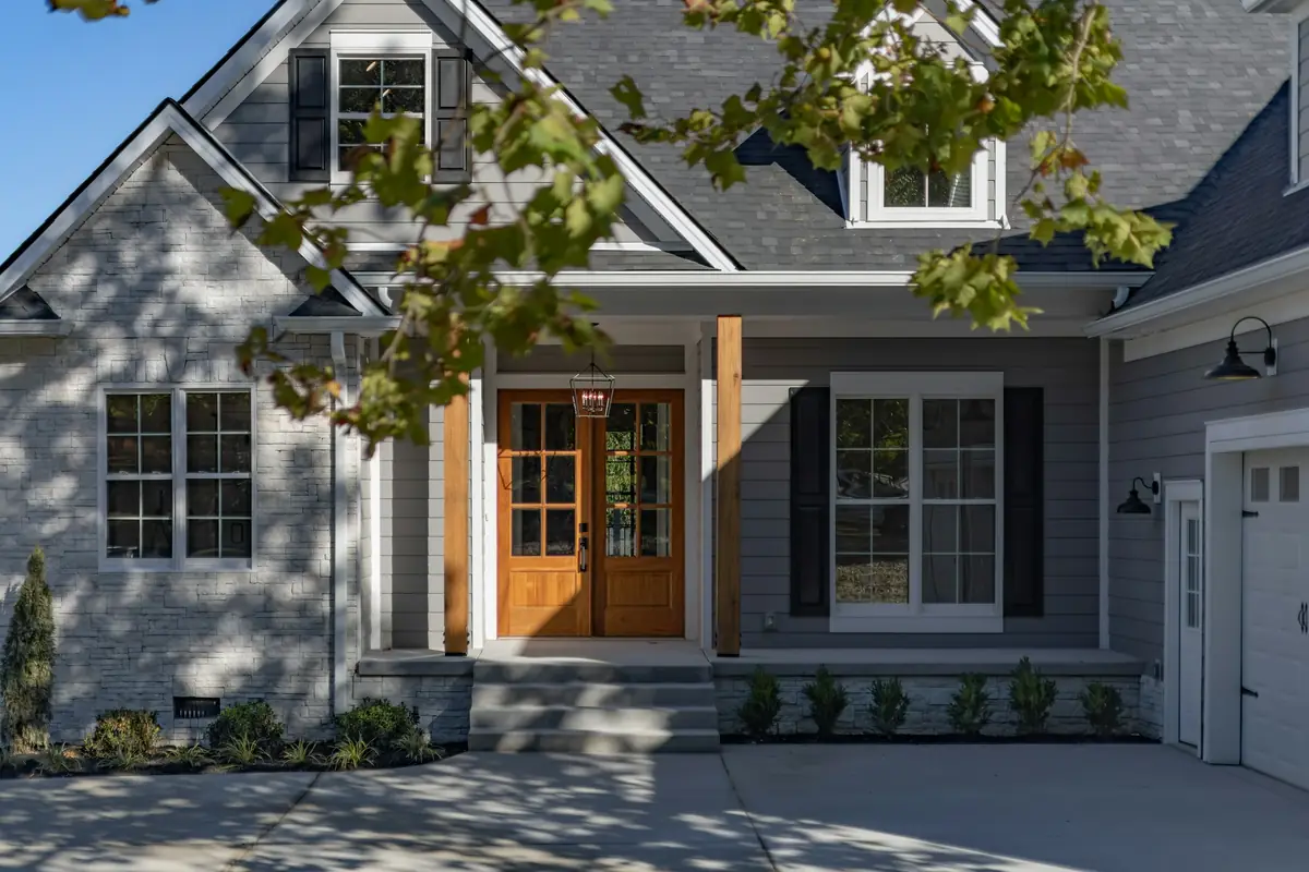 House entry with a light stone gable, gray lap siding, black shutters and a stained wood double door
