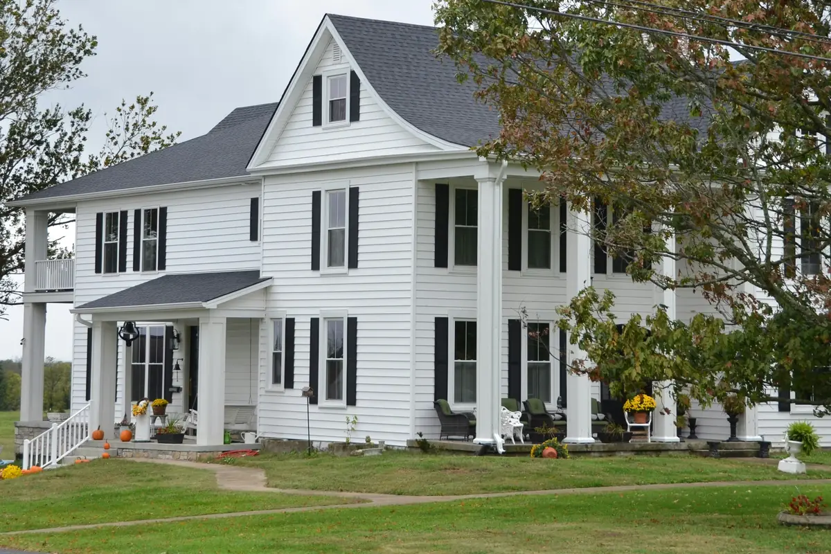 White two-story farmhouse with black shutters, a gray roof and a two-level columned porch with pumpkins