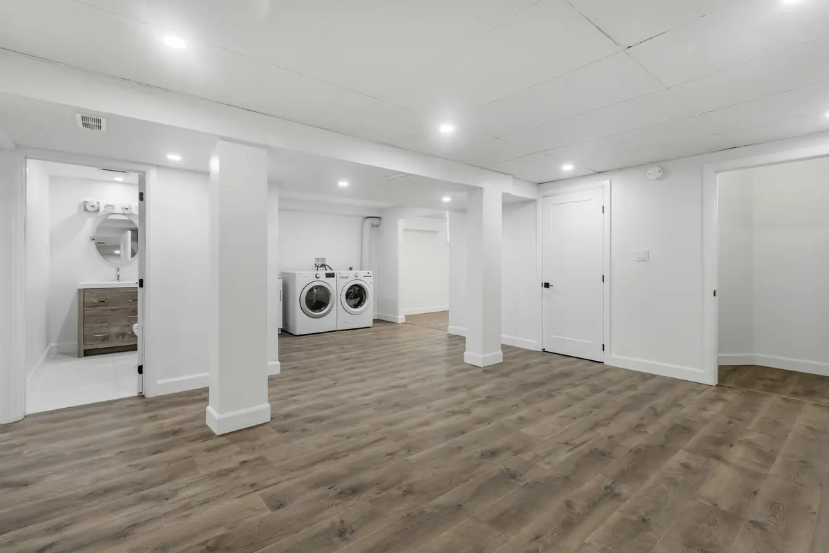 Finished basement with white walls and columns, a washer and dryer in an alcove and wide vinyl plank floors