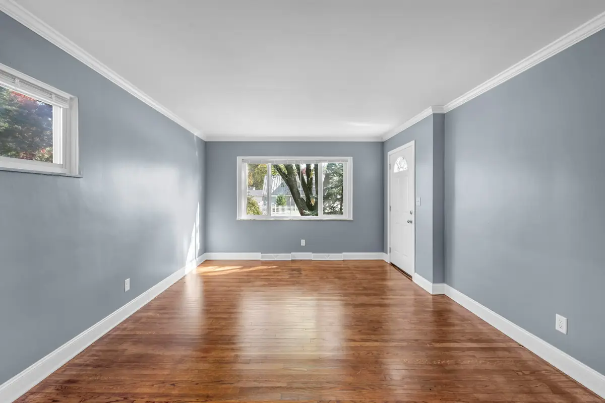 Long empty living room with blue-gray walls, white crown molding and baseboards and a dark wood floor