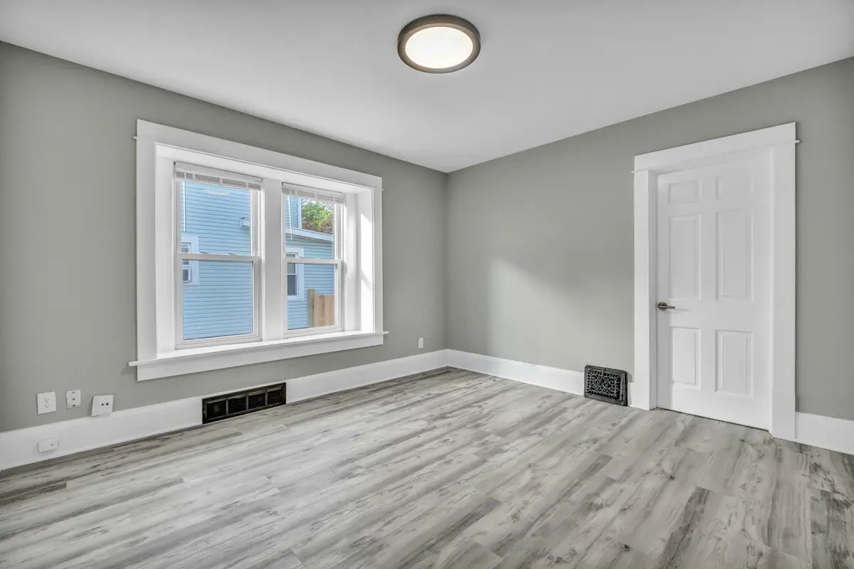 Empty bedroom with light gray walls, white window and door trim, a six-panel door and gray plank flooring