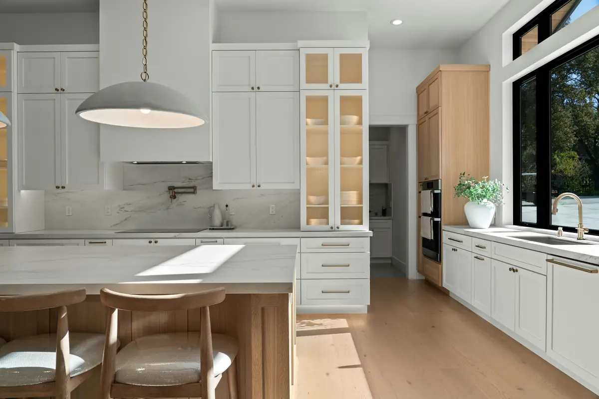 White kitchen with glass-front upper cabinets, a marble backsplash, a white-oak island and two wood stools